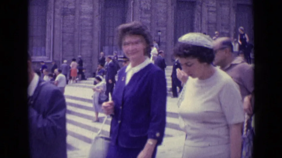 1962 Vatican City home-movie frame showing women in blue and white dresses walking close to the camera beside busy stone steps.