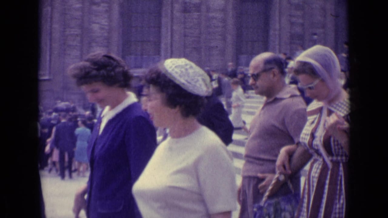 1962 Vatican City frame showing women in blue and white walking among visitors on broad steps near monumental stone architecture.
