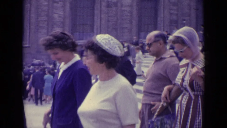 1962 Vatican City frame showing women in blue and white walking among visitors on broad steps near monumental stone architecture.