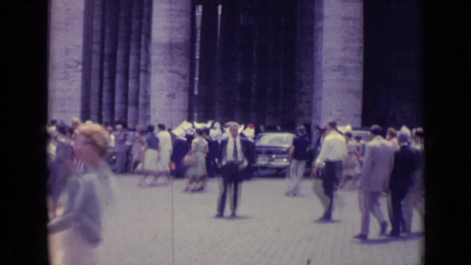 1962 Vatican City home-movie frame showing tourists and pedestrians moving across a square in front of tall stone columns.