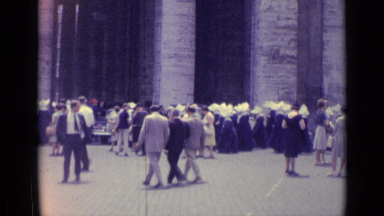 1962 Vatican City frame with pedestrians, nuns in traditional habits, and parked cars beside a monumental stone facade.