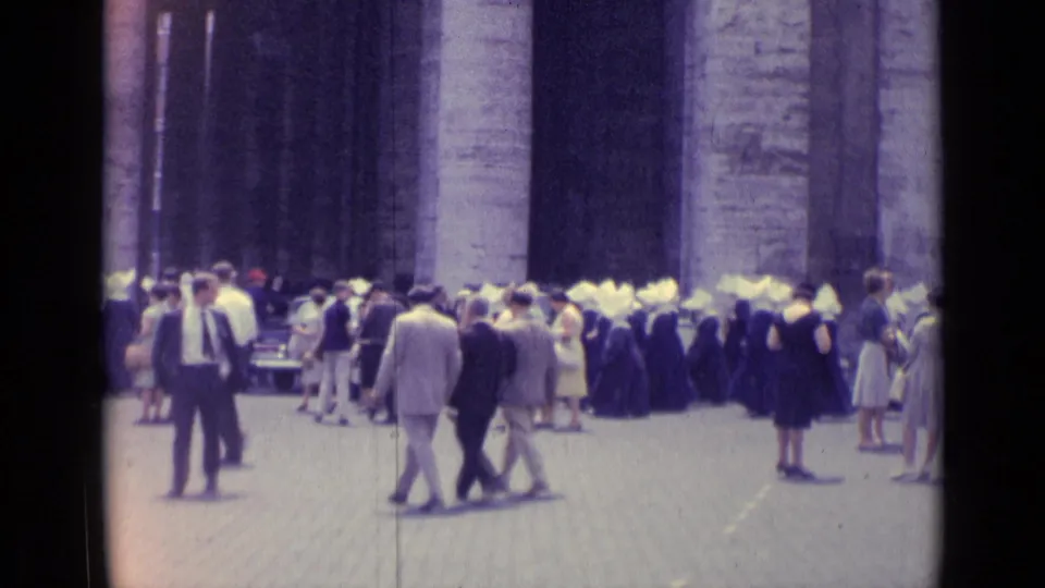 1962 Vatican City frame with pedestrians, nuns in traditional habits, and parked cars beside a monumental stone facade.