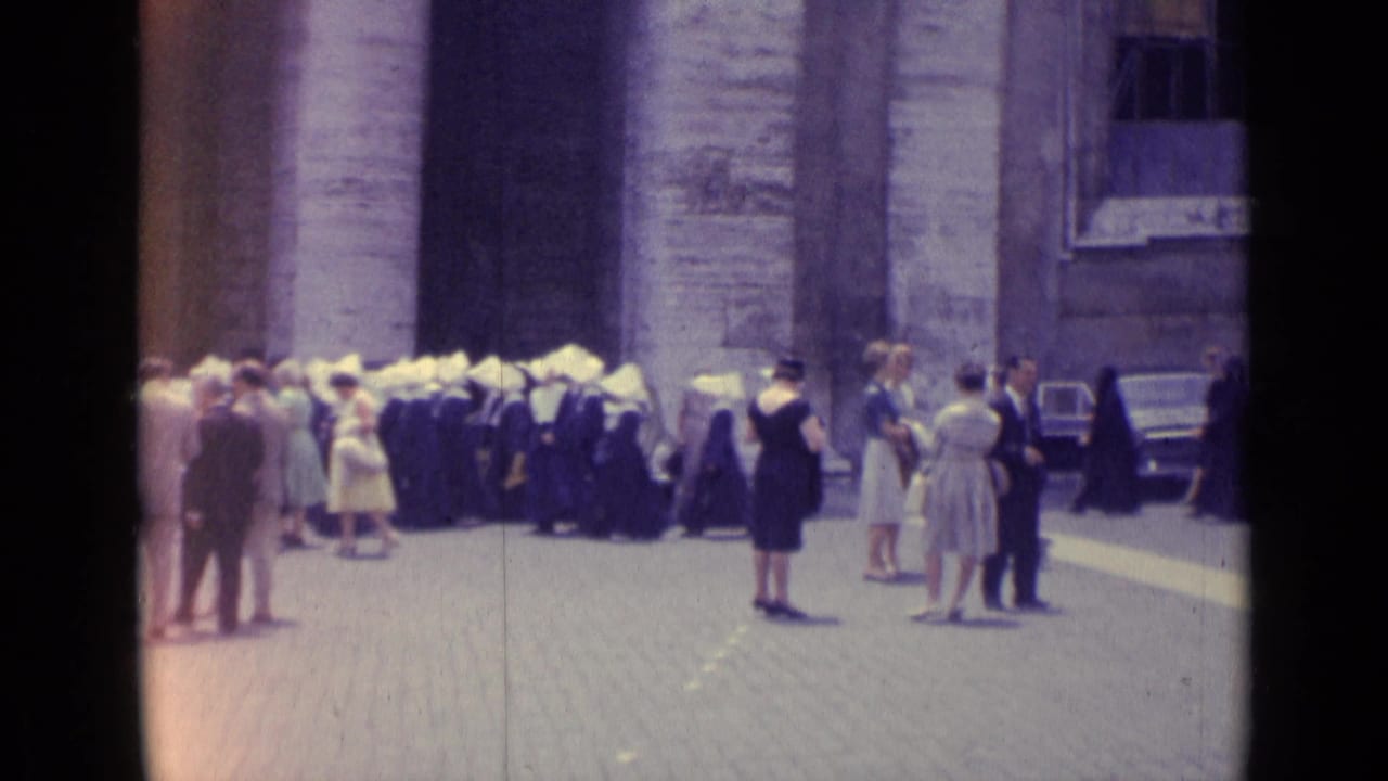 1962 Vatican City home-movie view of nuns, visitors, and pedestrians near parked cars and stone architecture.