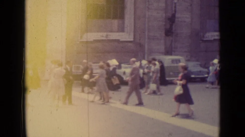 1962 Vatican City home-movie frame showing pedestrians near stone buildings and parked cars, with heavy flare at the left edge.