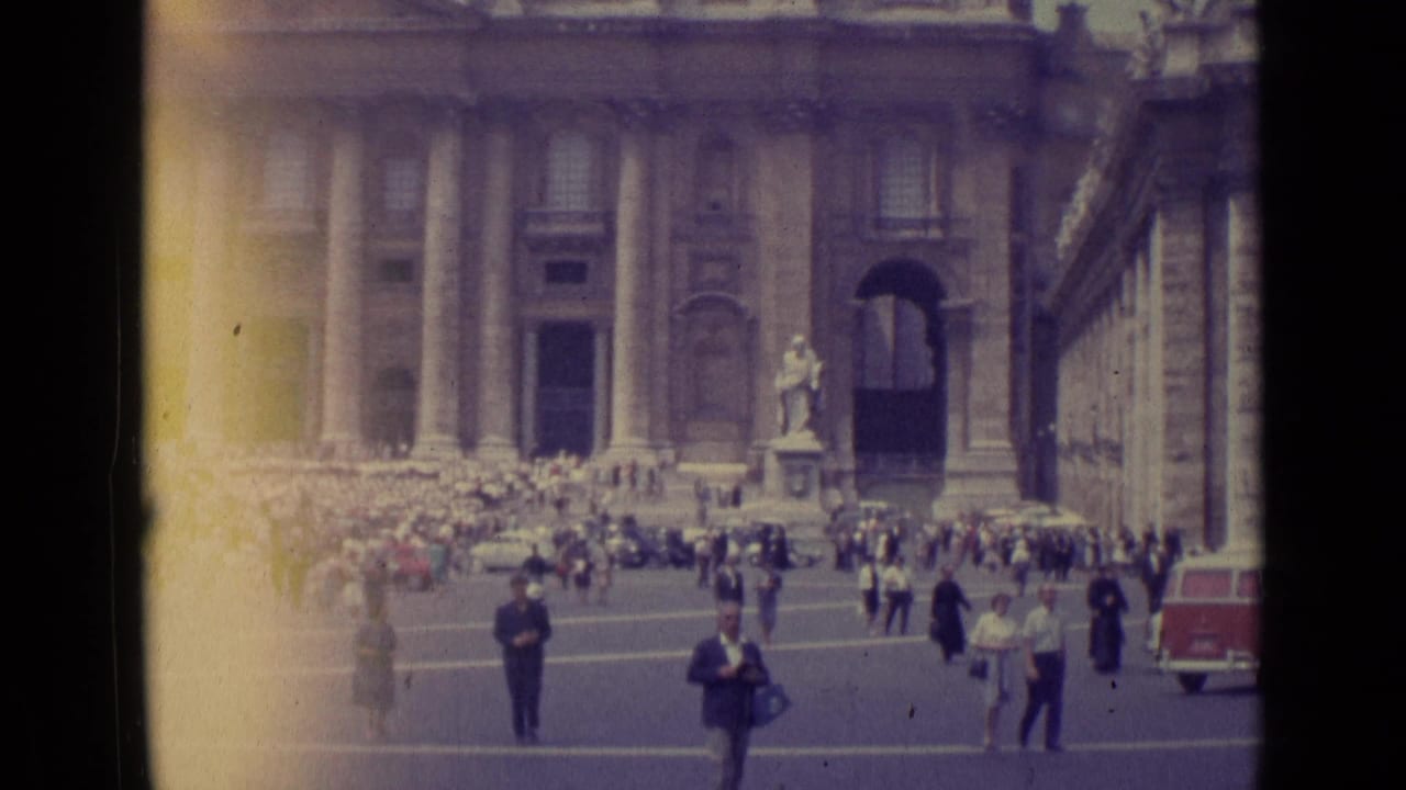 1962 Vatican City frame showing St. Peter's Basilica, groups of visitors, foreground pedestrians, and a red-and-white van at the edge.