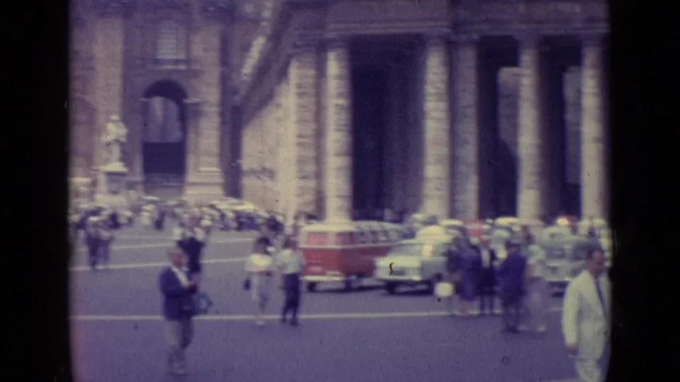 1962 Vatican City 8mm frame showing tourists and cars near a colonnaded square, with a red-and-white van at center left.
