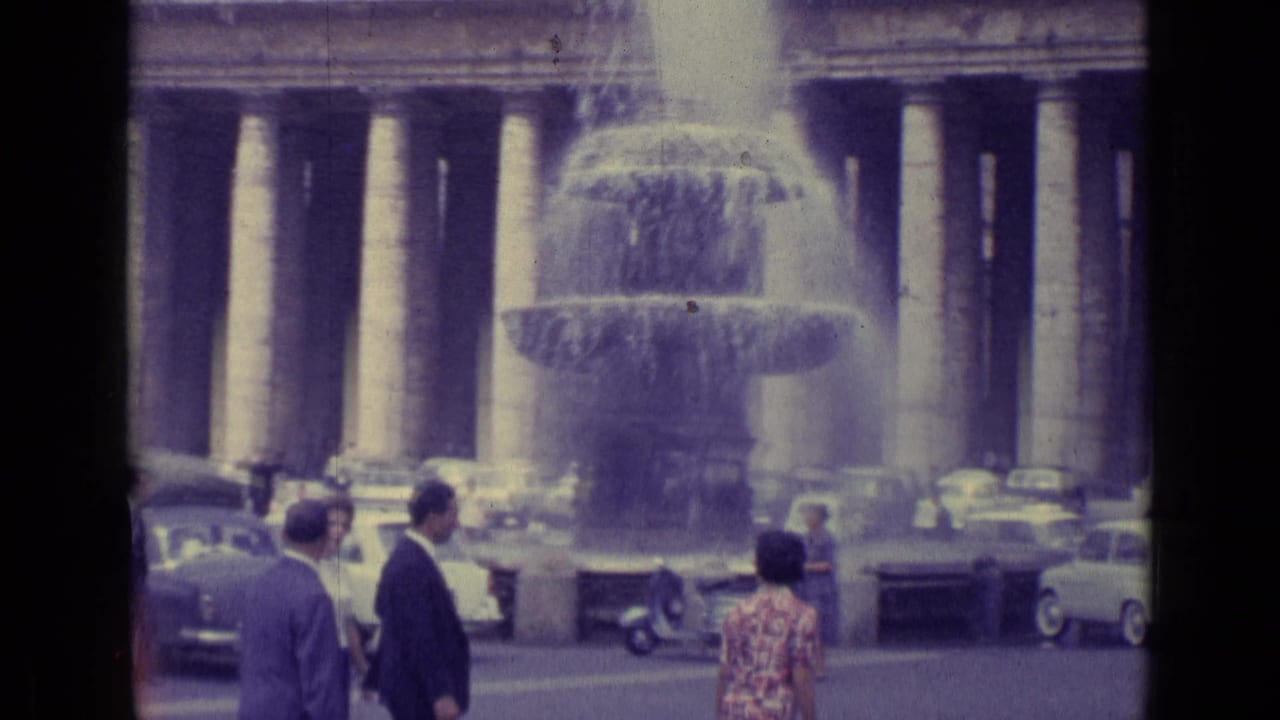 1962 Vatican City 8mm frame showing a large fountain, visitors, cars, and the surrounding colonnade.