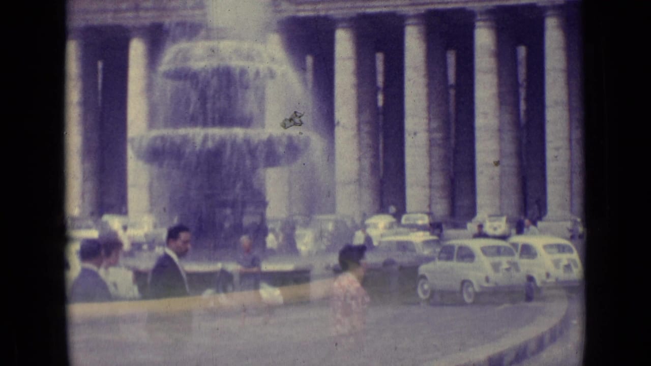 1962 Vatican City street scene with pedestrians near a large fountain, classical columns, and vintage cars around a plaza.