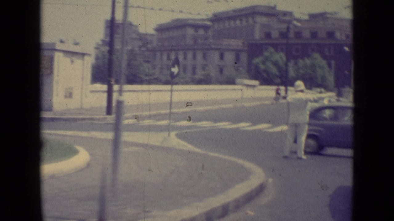 1962 Vatican City roadway view with a traffic policeman in white directing cars near formal buildings and street signs.