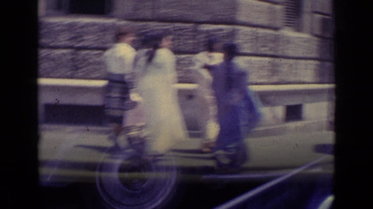 Women continue across the street as a blurred vehicle passes nearby.