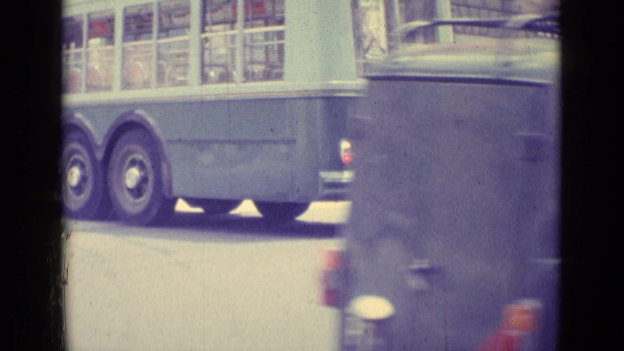 A large bus and a foreground car pass through the 1962 Vatican City street view, partially obscuring the pedestrian crossing scene.