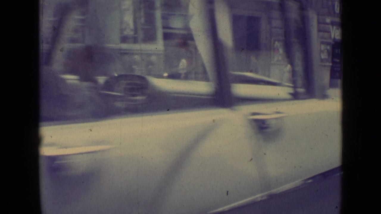 A foreground car moves past bus windows and street poles in a soft, grainy 8mm Vatican City street frame from 1962.
