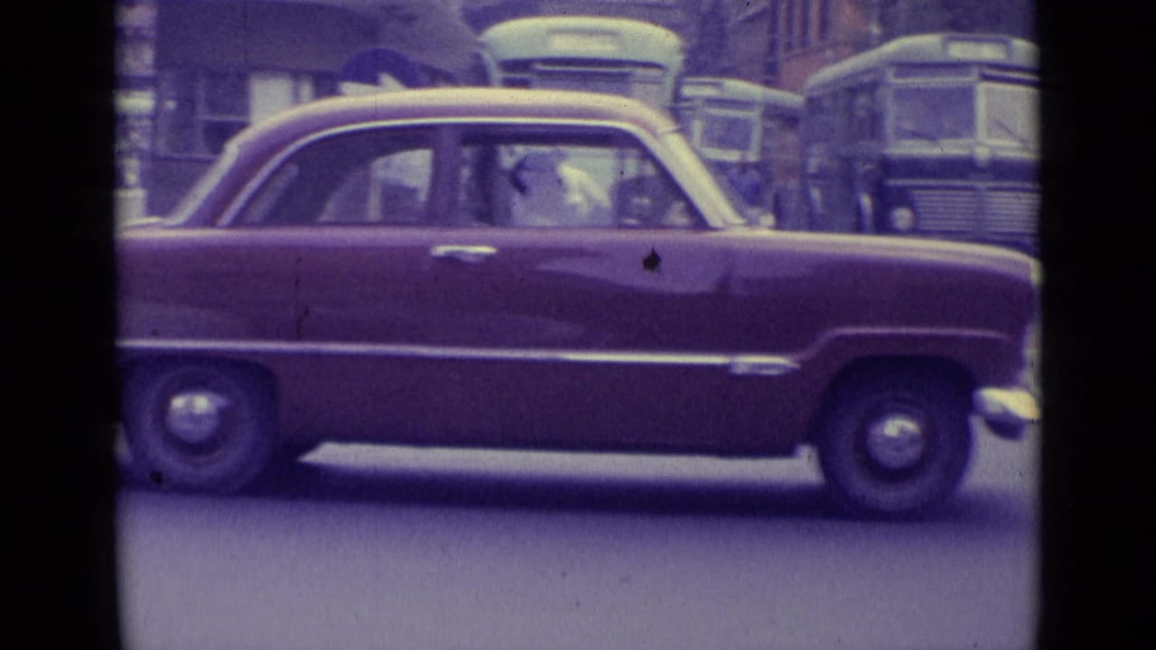 Maroon sedan in side view with buses and street traffic behind it.
