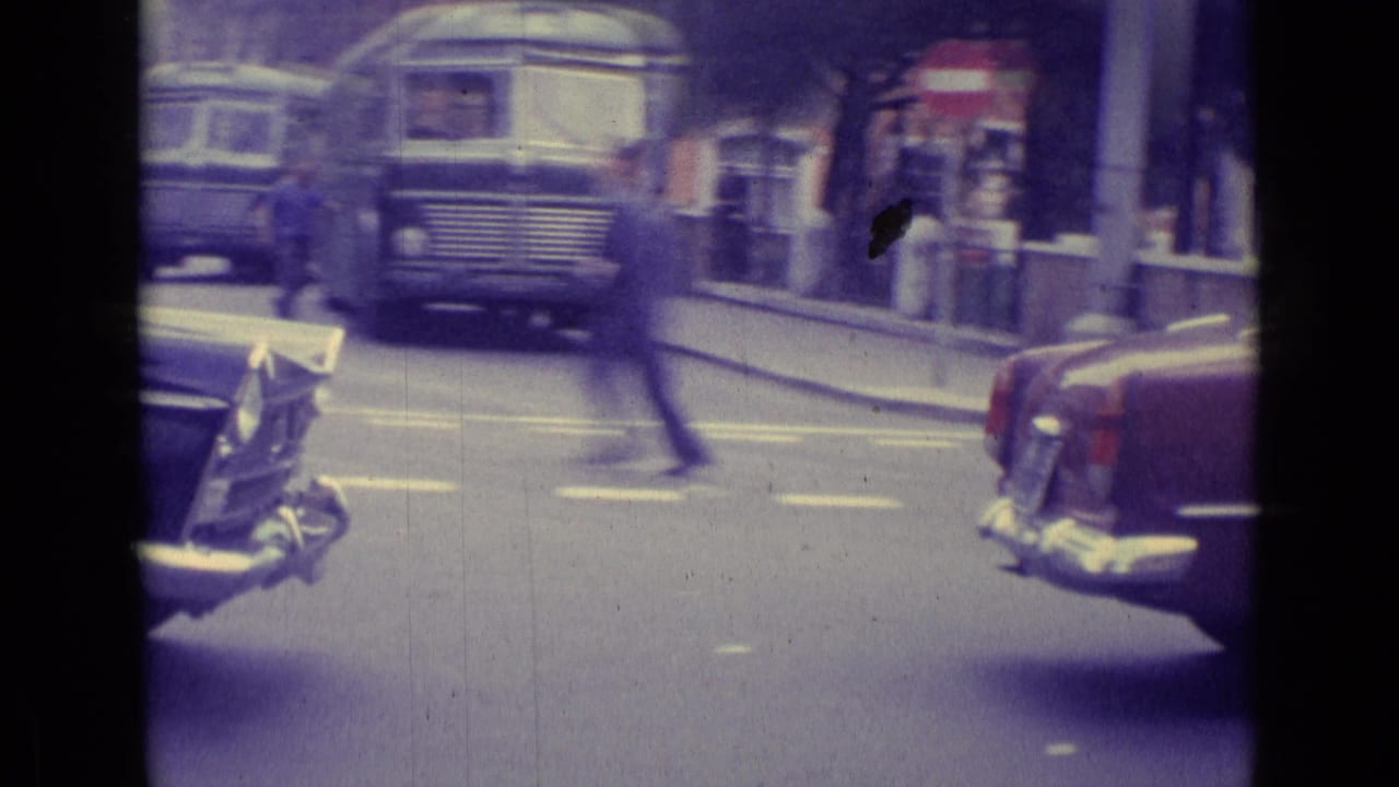 1962 Vatican City home-movie street scene with a bus facing camera, classic cars at both sides, and a pedestrian crossing in motion blur.