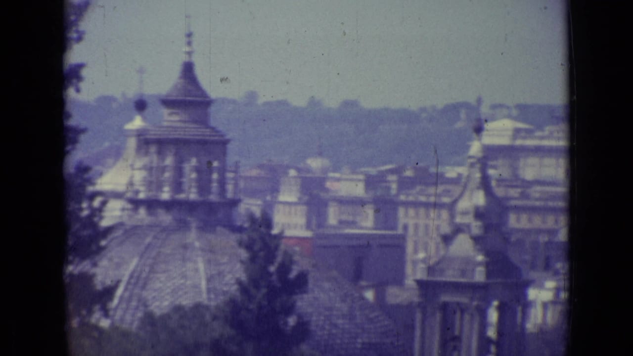 1962 Vatican City travel frame showing an elevated view across historic rooftops, domes, trees, and a hazy skyline.