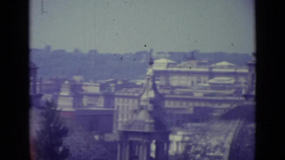 1962 8mm Vatican City rooftop view with hazy buildings, domes, spires, and visible film gate edges.