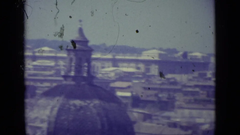 1962 Vatican City roofscape with a large foreground dome shape, spire, hazy skyline, and blue-purple film cast.