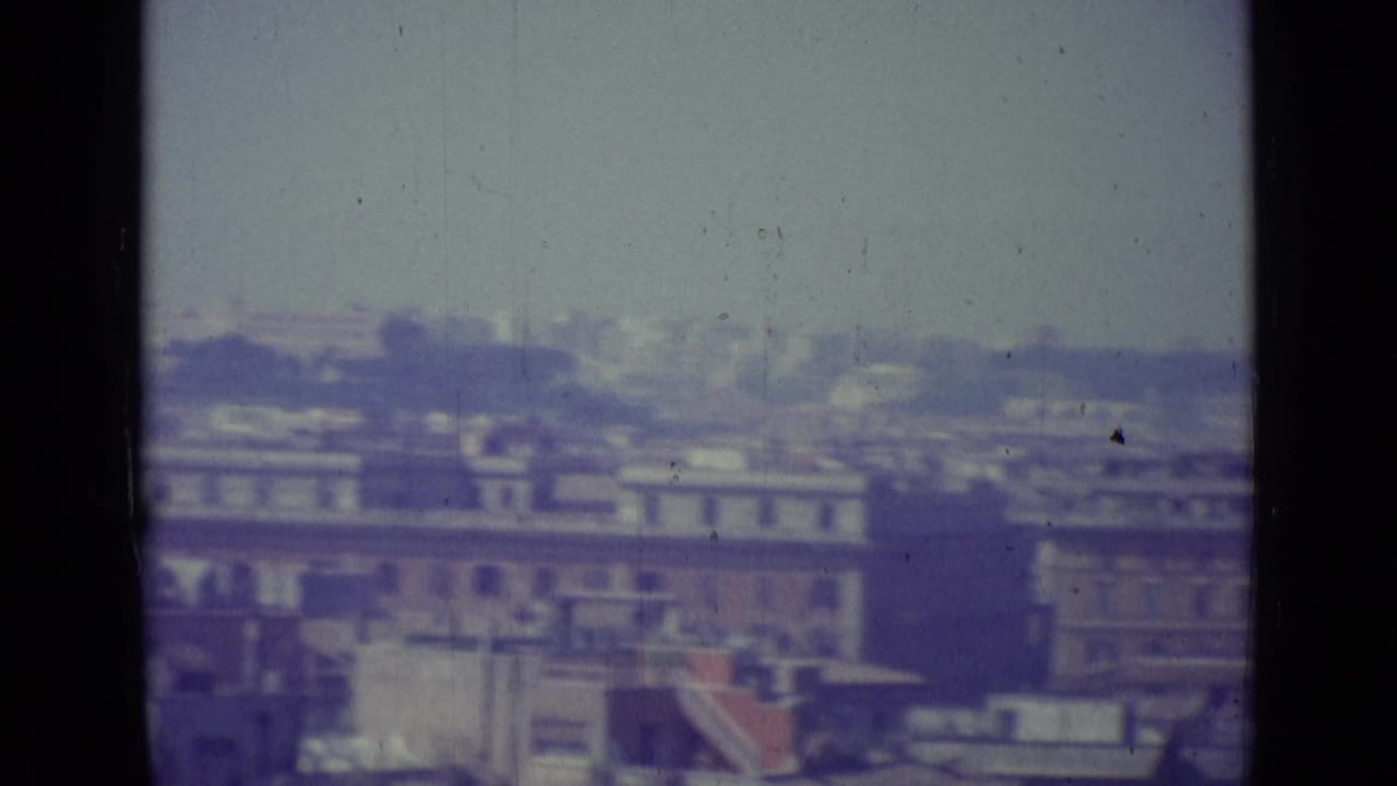 End of a 1962 Vatican City pan showing clustered rooftops, distant structures, haze, and prominent film gate borders.