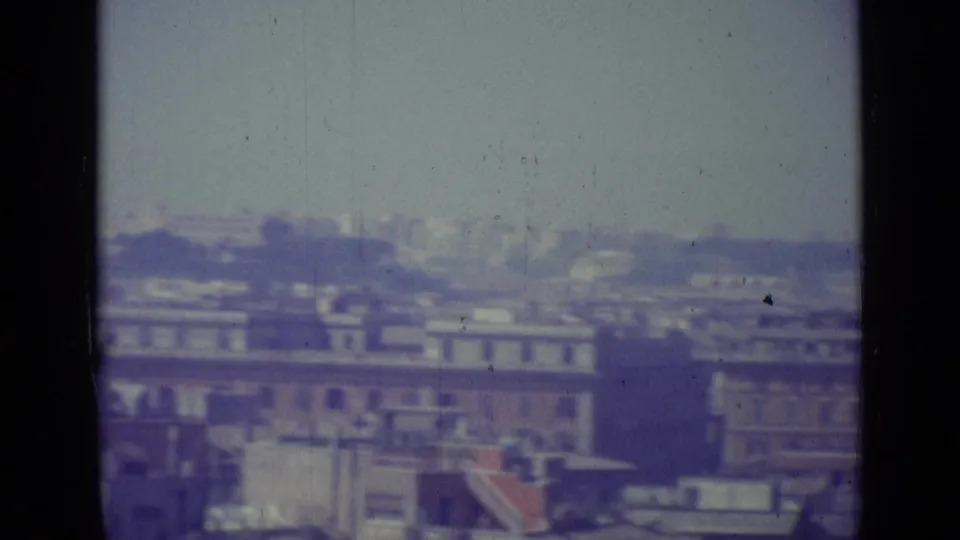 End of a 1962 Vatican City pan showing clustered rooftops, distant structures, haze, and prominent film gate borders.