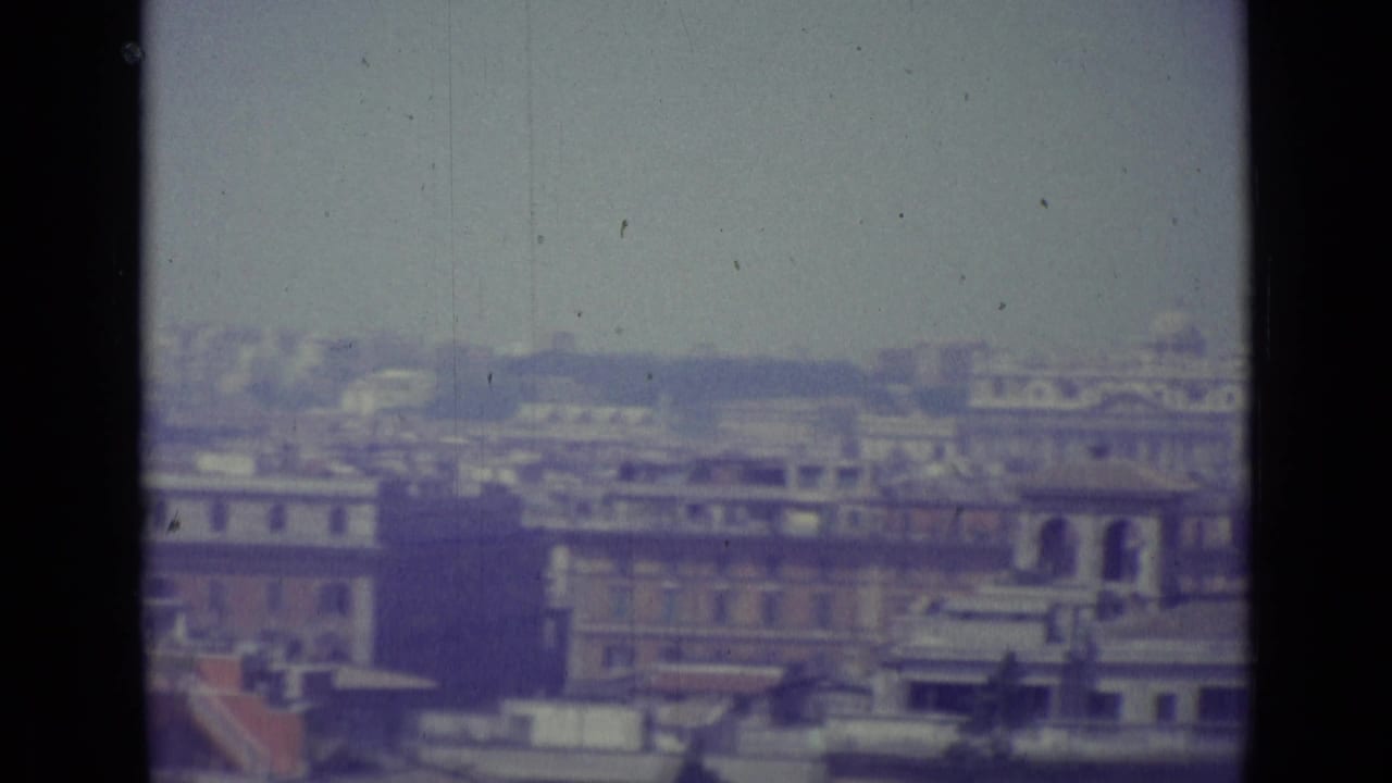 Hazy city skyline with rooftops and a distant dome seen through 8mm film borders.