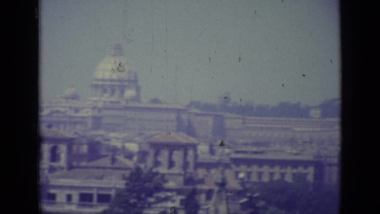 Distant domed landmark above a broad cityscape with rooftops and film scratches.