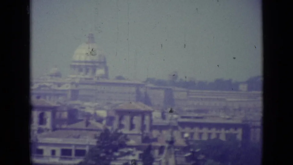 1962 Vatican City panorama showing a prominent distant dome, layered rooftops, haze, and vertical scratches on 8mm film.