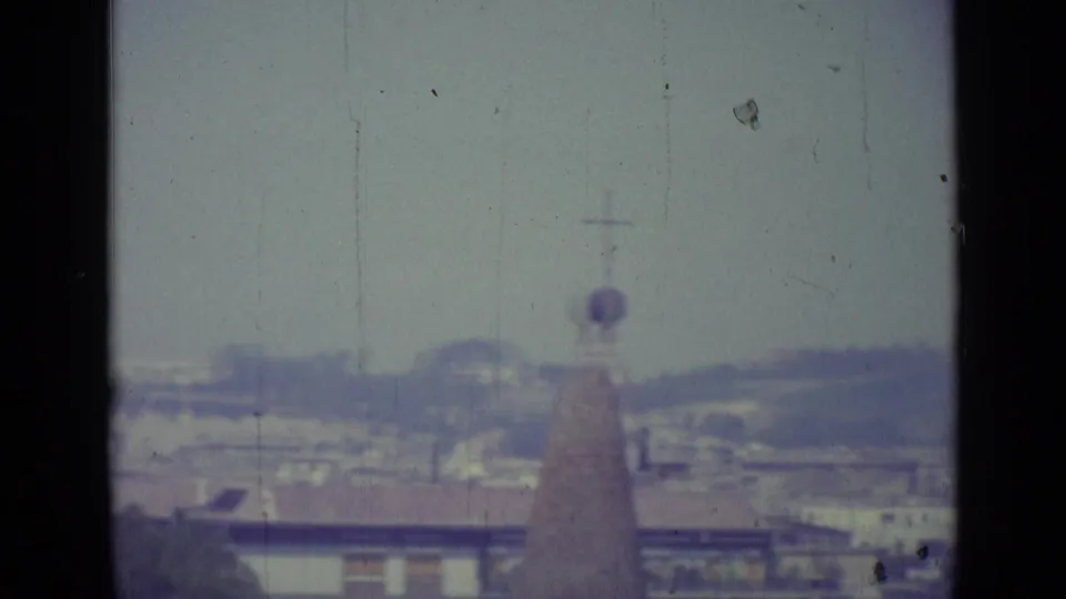 1962 Vatican City view with a cross-topped spire, low rooftops, distant dome-like forms, and visible 8mm film wear.
