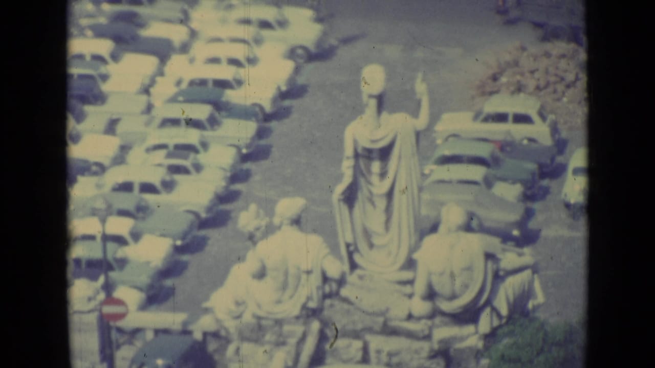 Statue group above rows of parked vintage cars and a roadway.