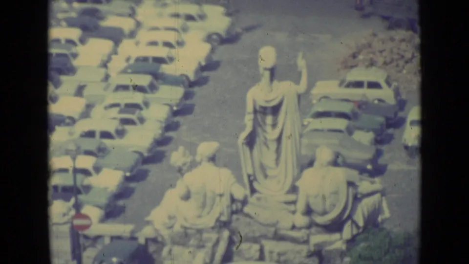1962 Vatican City frame looking down on a raised statue group beside rows of compact vintage cars.