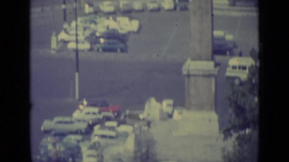 1962 Vatican City frame showing cars and a stone monument base from an elevated, hazy visitor viewpoint.