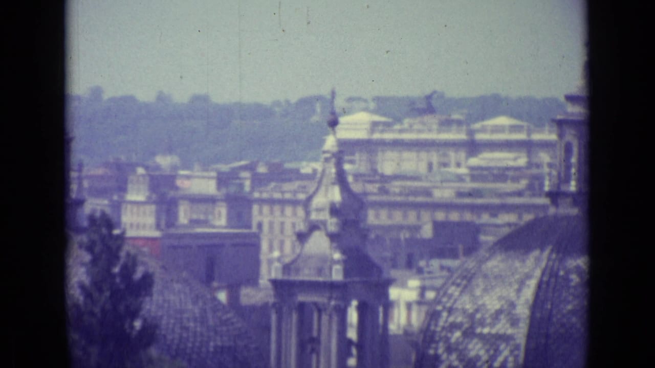1962 Vatican City view across domed rooftops, tower details, distant buildings, and a pale skyline on grainy 8mm film.