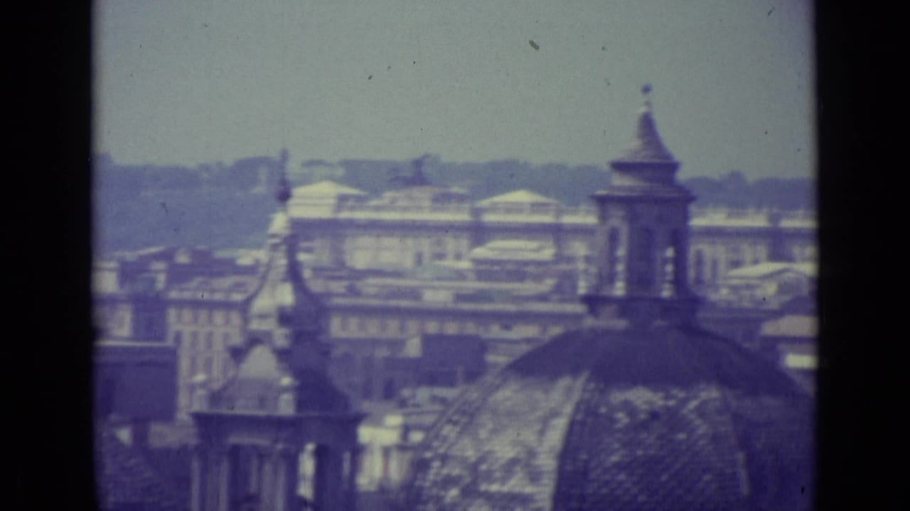 Vatican City home-movie frame showing a domed roof, tower, layered rooftops, and distant buildings under a hazy sky.