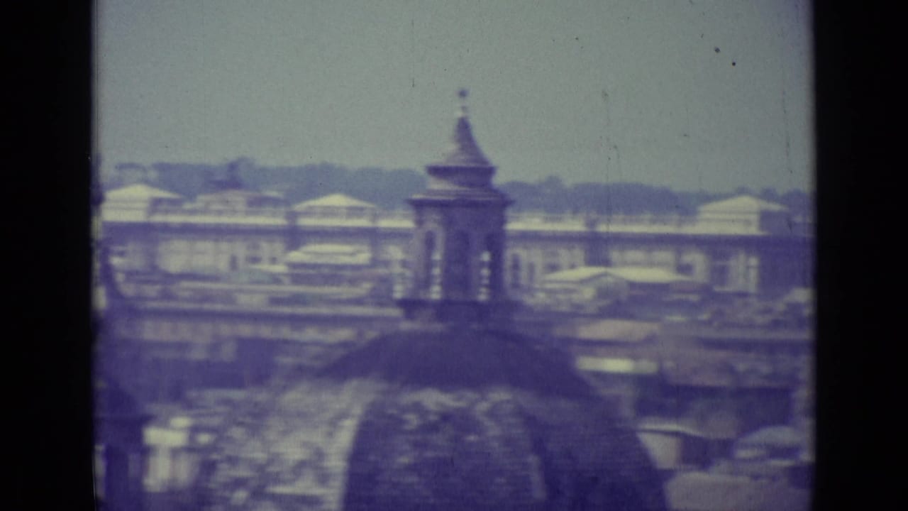 1962 8mm Vatican City view with historic rooftops, a small dome or tower, haze, faded color, and visible film gate edges.