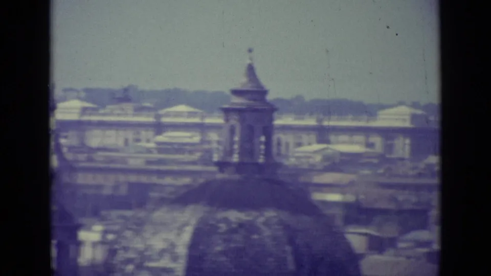 1962 8mm Vatican City view with historic rooftops, a small dome or tower, haze, faded color, and visible film gate edges.