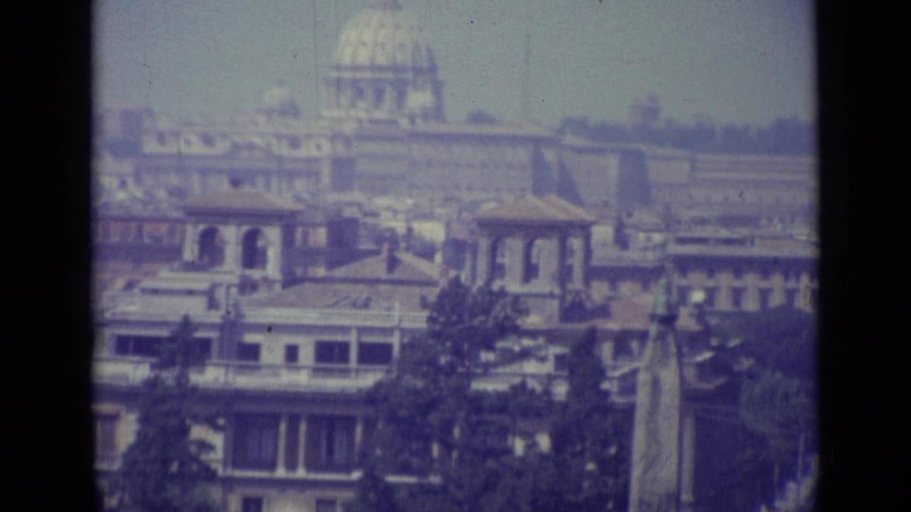 St. Peter's Basilica dome above Vatican rooftops and trees in a soft color frame.