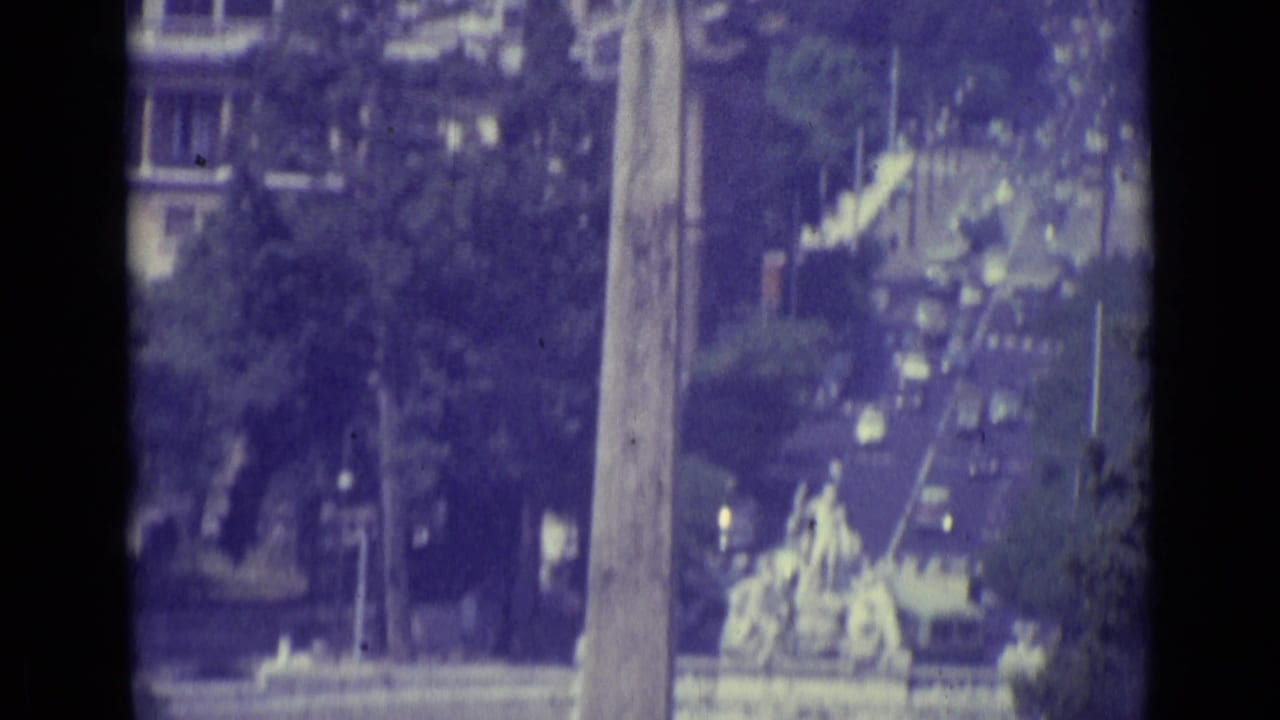 1962 Vatican City close view of a tall obelisk-like monument, trees, and soft urban detail in faded 8mm color.