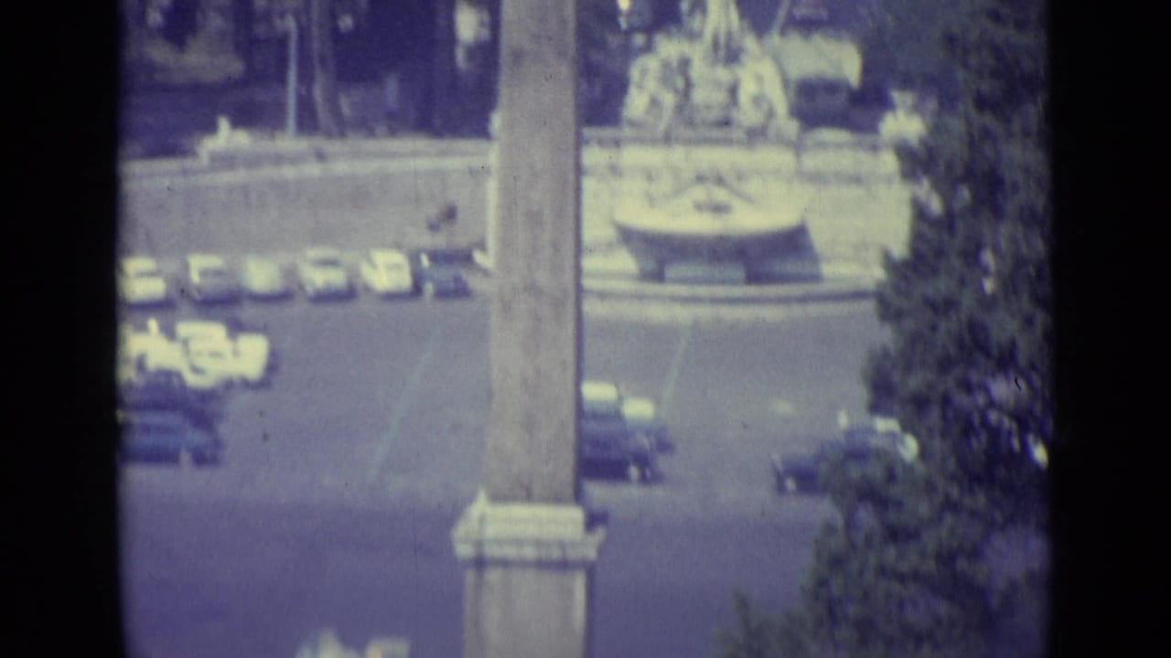 Elevated view of an obelisk, traffic, trees, and a fountain area in a sunlit square.