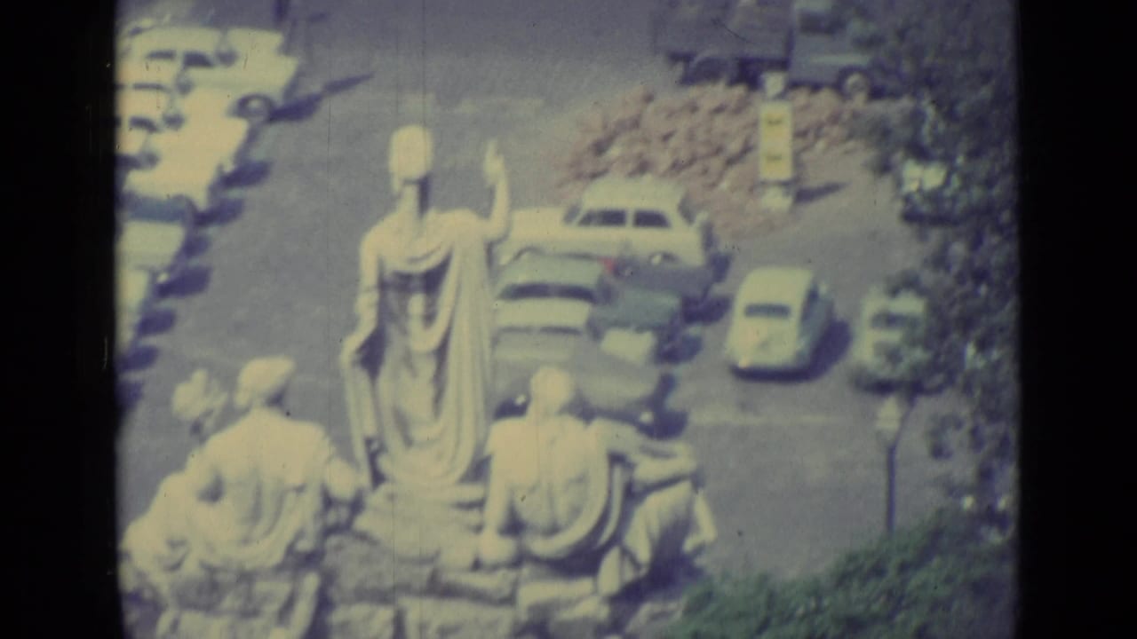 1962 Vatican City frame showing classical statues overlooking cars, trees, and a sunlit public square.