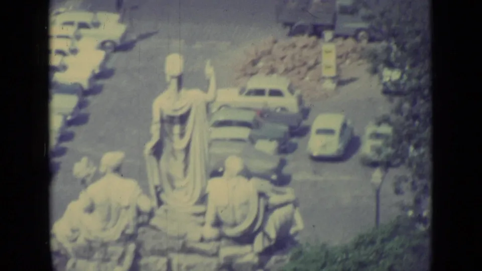 1962 Vatican City frame showing classical statues overlooking cars, trees, and a sunlit public square.