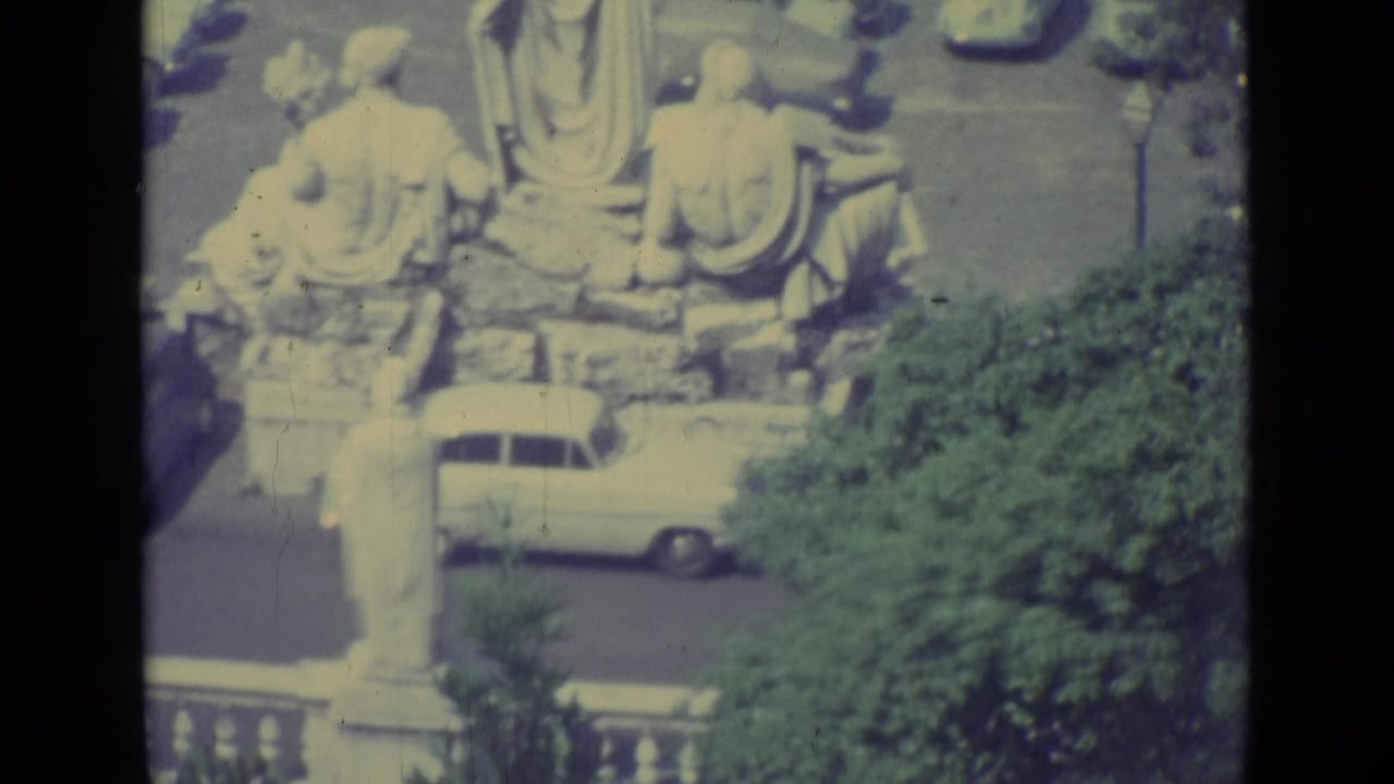 1962 Vatican City frame with classical statues, the lower obelisk area, cars, trees, and a balustrade from an elevated viewpoint.