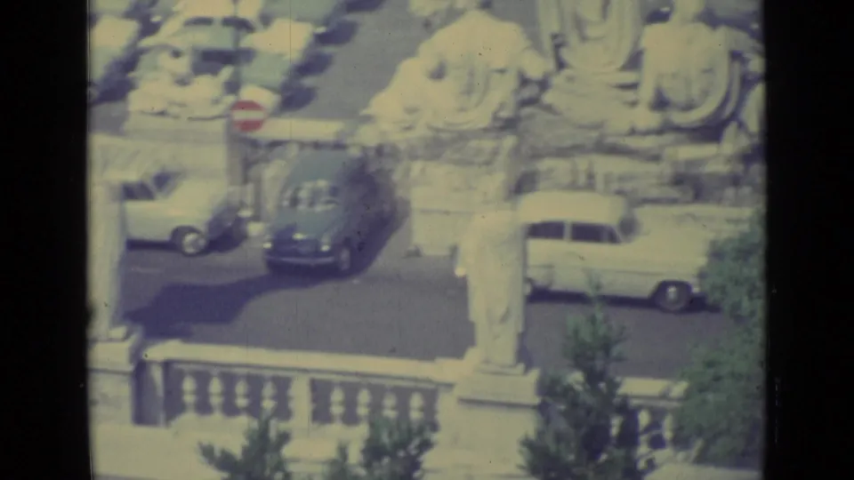 1962 Vatican City home-movie frame showing a sunlit courtyard with classical statues, cars, a red stop sign, and stone railing.