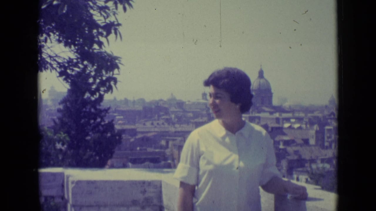 Woman in a white shirt standing by a terrace with a domed skyline behind her.