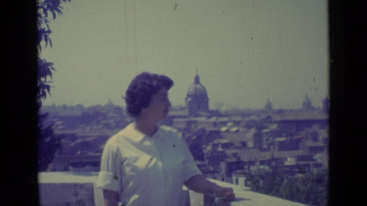 The woman appears in profile on a balcony above Vatican City, with rooftops and a prominent dome under a hazy sky.