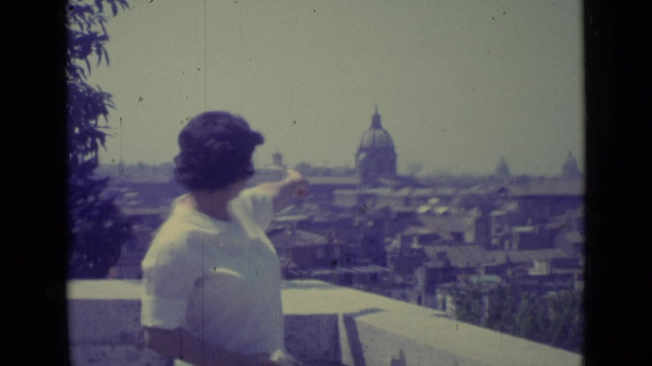 Woman on a terrace points toward a domed church across a hazy city skyline.