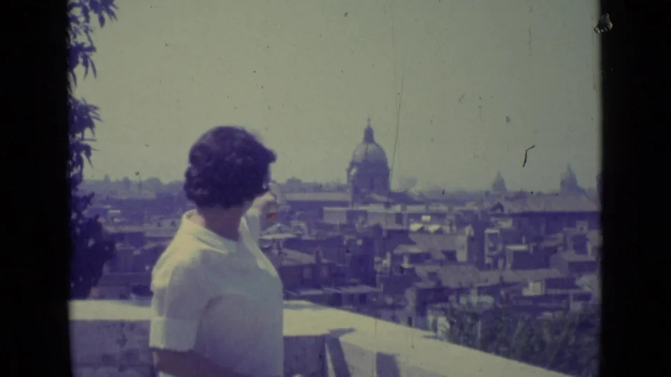 The woman stands on a terrace in Vatican City, looking toward a domed church rising above the 1962 cityscape.