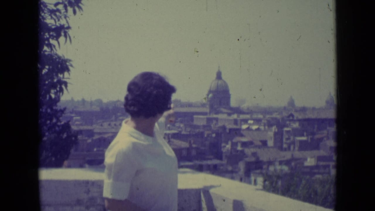 A woman in a white blouse stands at a Vatican City terrace as the domed church and surrounding rooftops remain in view.
