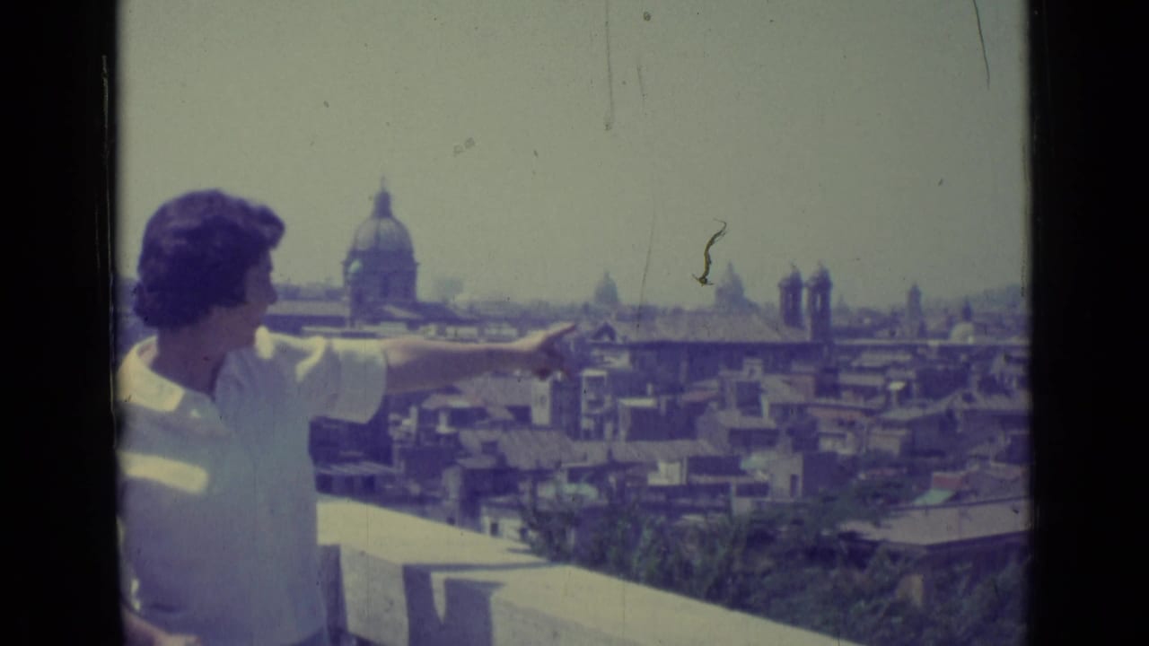 Woman in a white blouse points from a balcony toward a distant domed skyline.