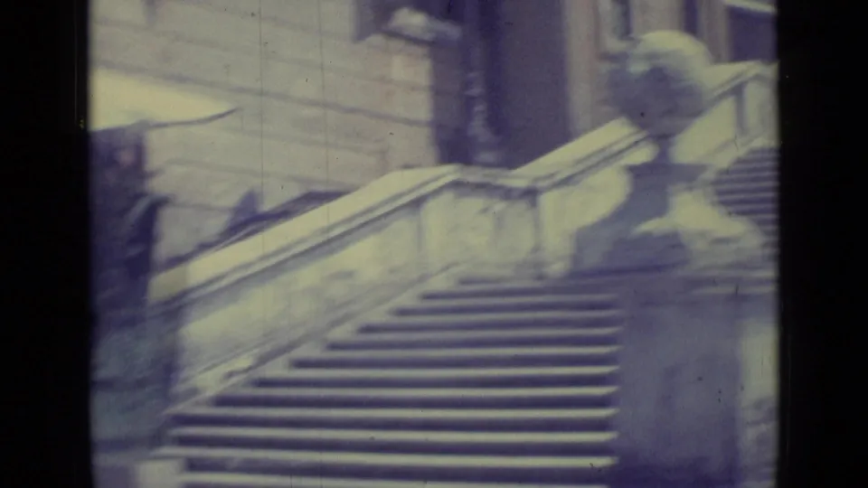 1962 Vatican City frame showing a uniformed guard standing near a carved pillar beside the grand stairway and stone balustrade.