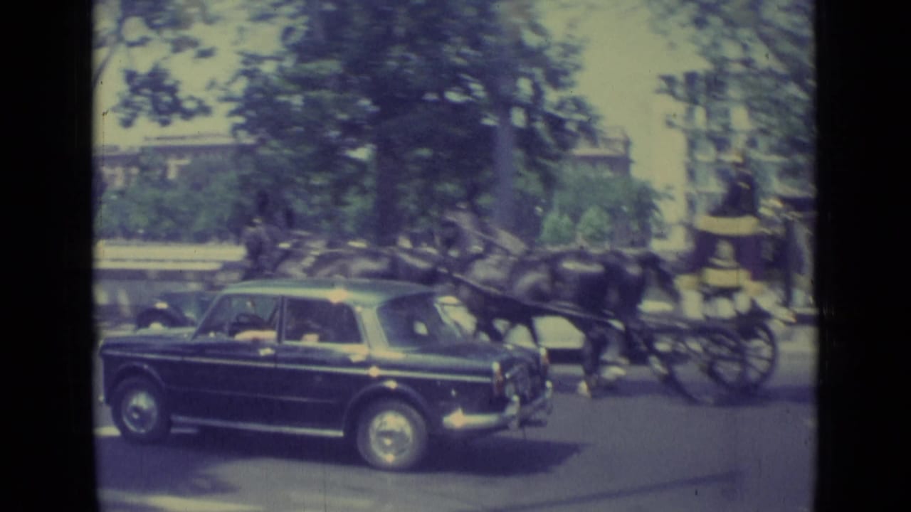 Black sedan on a city street beside a horse-drawn carriage and trees.