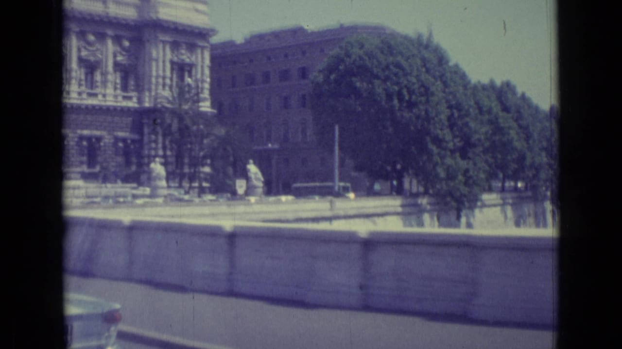 Final frame shows ornate stone architecture, a tree-lined riverside edge, pedestrians at a distance, and the top of a passing car.